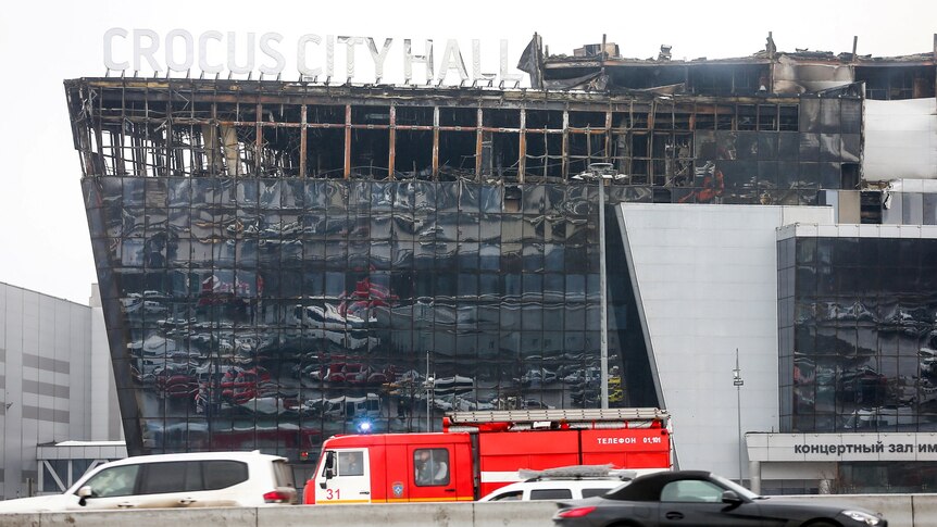A view showing a building that has been burned with cars and an emergency vehicle in front of it.