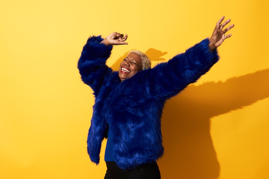 Black older woman in blue fur coat smiling with arms raised