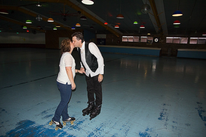 A couple share a kiss on a roller skating rink