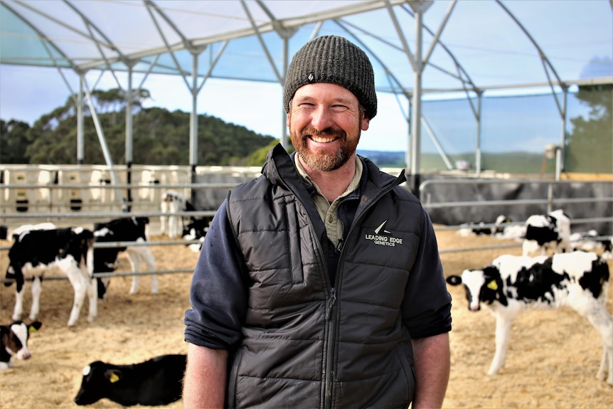 Photo of a man smiling in front of dairy cows.