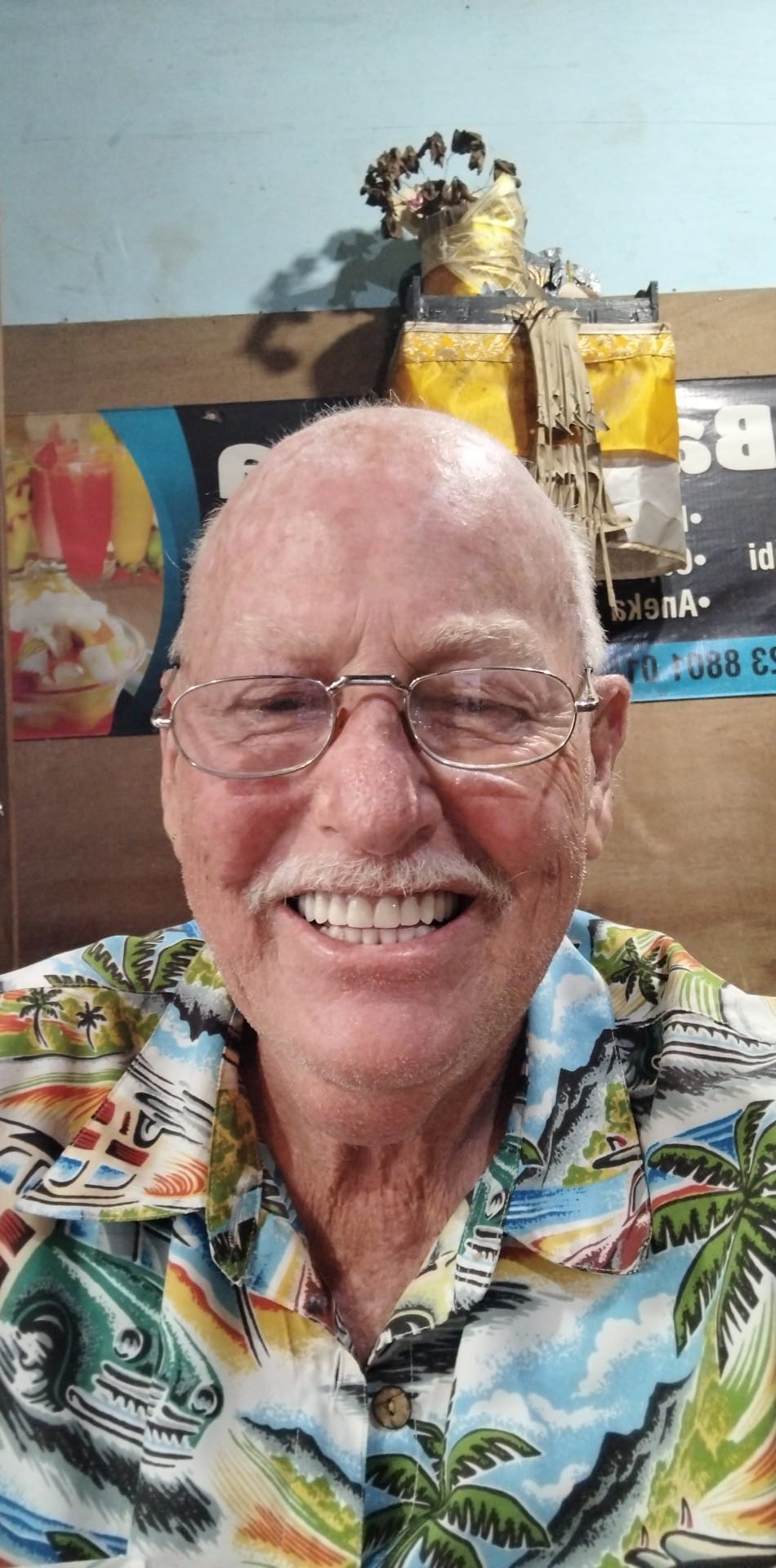 Homem com camisa colorida, bigode e óculos.