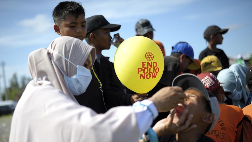 A woman giving an oral vaccination to a kid wearing hat