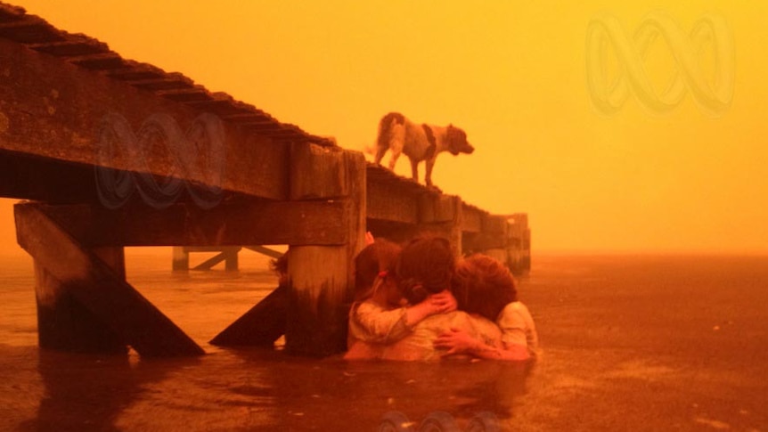 Families huddle in the water next to a jetty during a bushfire sweeping through Dunalley.