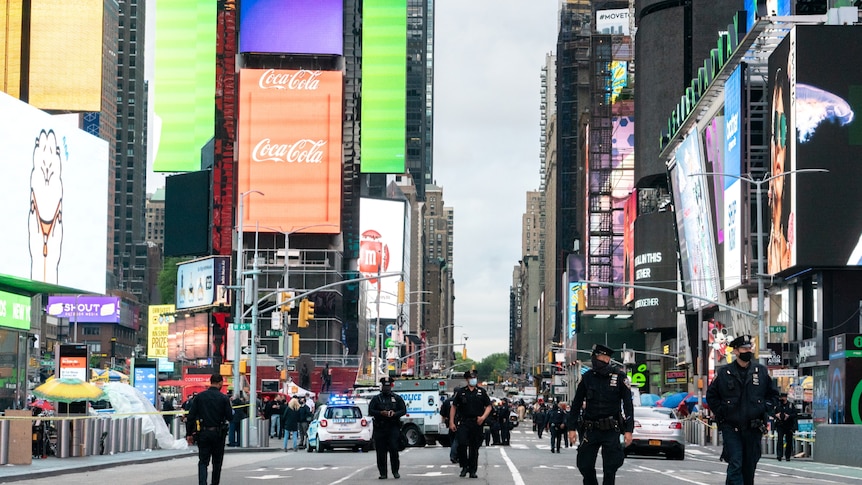 Five police officers are seen in the foreground of an image of New York's Times Square, walking on road with billboards behind 