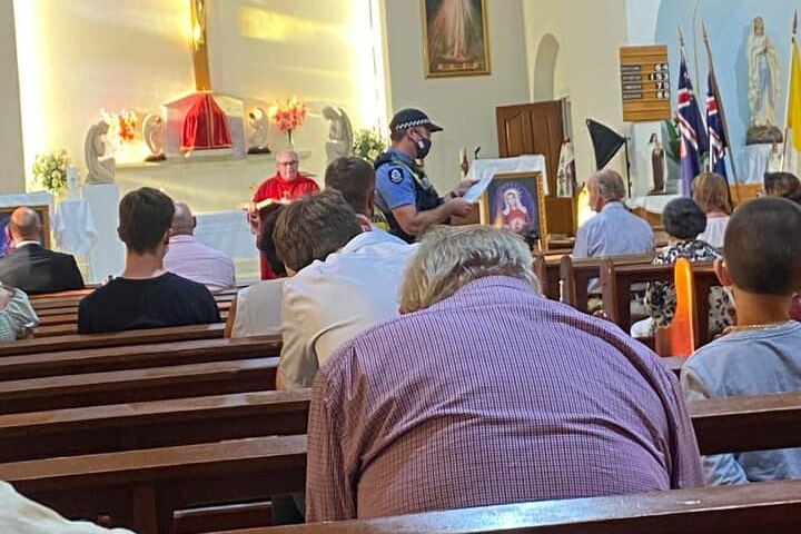 A police officer does a mask check during a Catholic church service