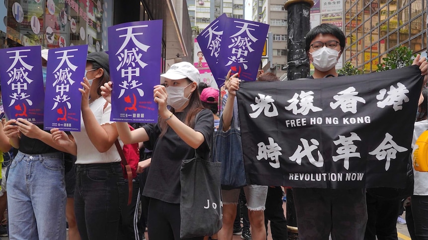 people with face masks on hold up signs in a streets in hong kong