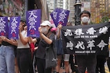 people with face masks on hold up signs in a streets in hong kong