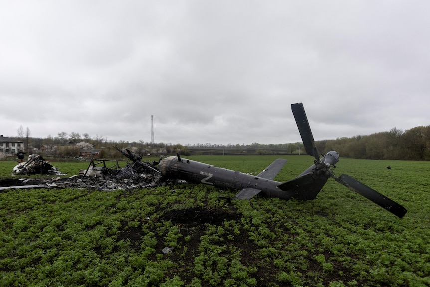 A destroyed Russian helicopter marked with the "Z" symbol is seen in a green field.