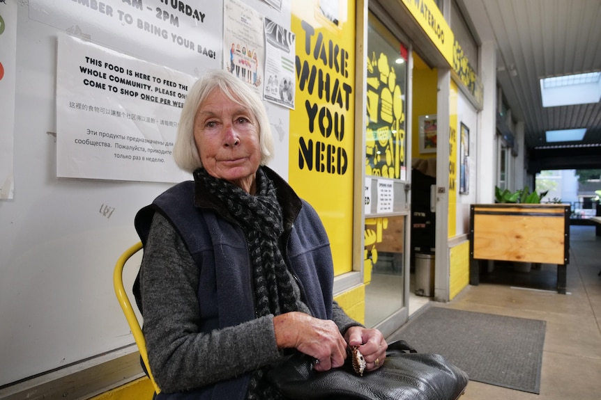 A woman sitting down on a yellow chair in the hallway of an indoor shopping centre outside an open door