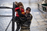 A volunteer carries a young girl to high ground after using a boat to rescue a woman and children.