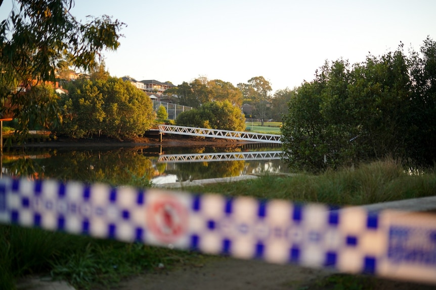 Police tape in front of a river and a bridge in the distance / police looking over the edge of a bridge with a river below