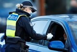 A female police officer with blonde hair wears a facemask and gloves as she checks the licence of a female driver in a blue car.