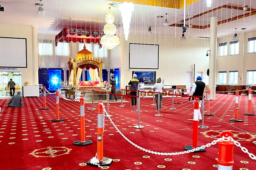 Several people stand in an attitude of prayer in front of a golden altar in a large, carpeted room.