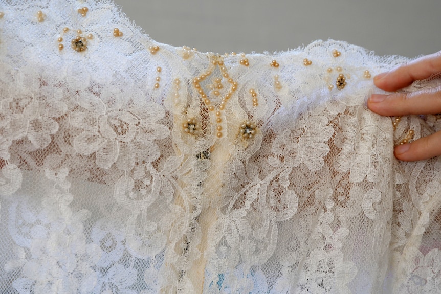 The top of a white lace dress with small pearl beading at the top