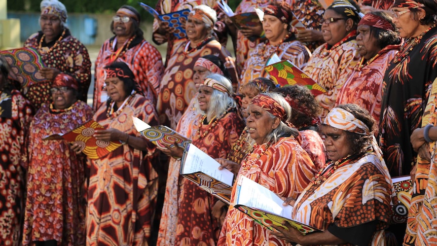 A choir of Australian Aboriginal women in colourful clothing printed with Aboriginal artwork.