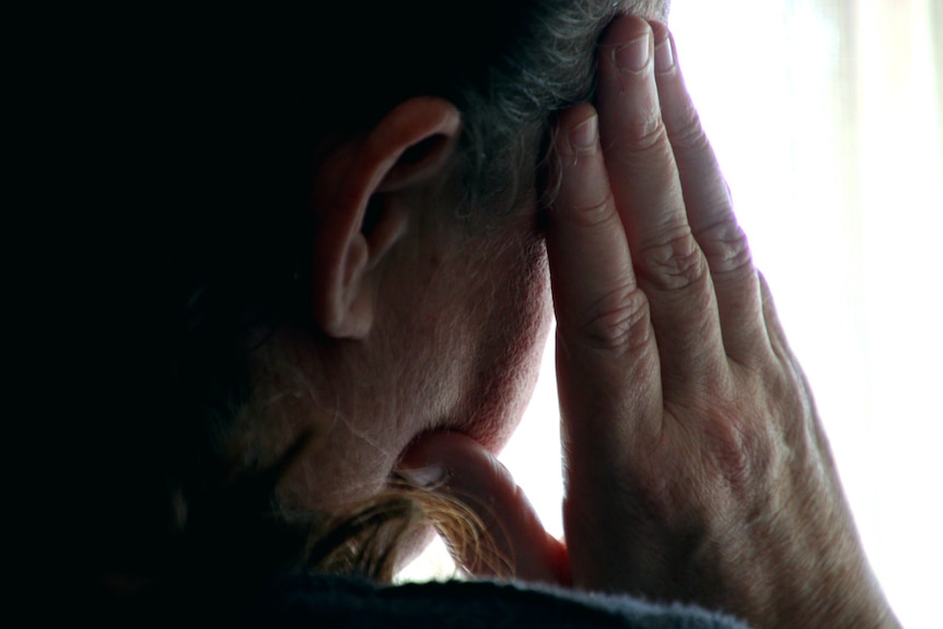 Close up of an anonymous woman pictured from behind with her hand on her head