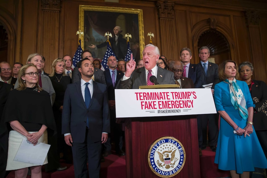 Group of US lawmakers stand as man in centre waves his finger in front of podium with sign 'Terminate Trump's fake emergency'