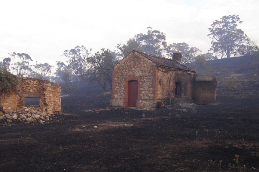 An old, stone frontier building damaged by fire in a burnt field.