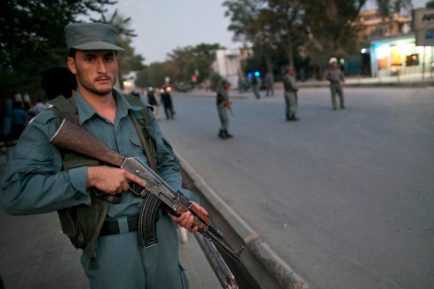 An Afghan policeman with gun over shoulder keeps watch near the house of Burhanuddin Rabbani