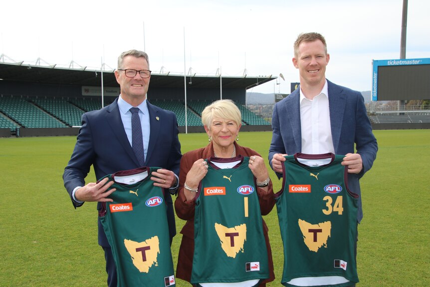 Two men and a woman hold up sporting guernseys.