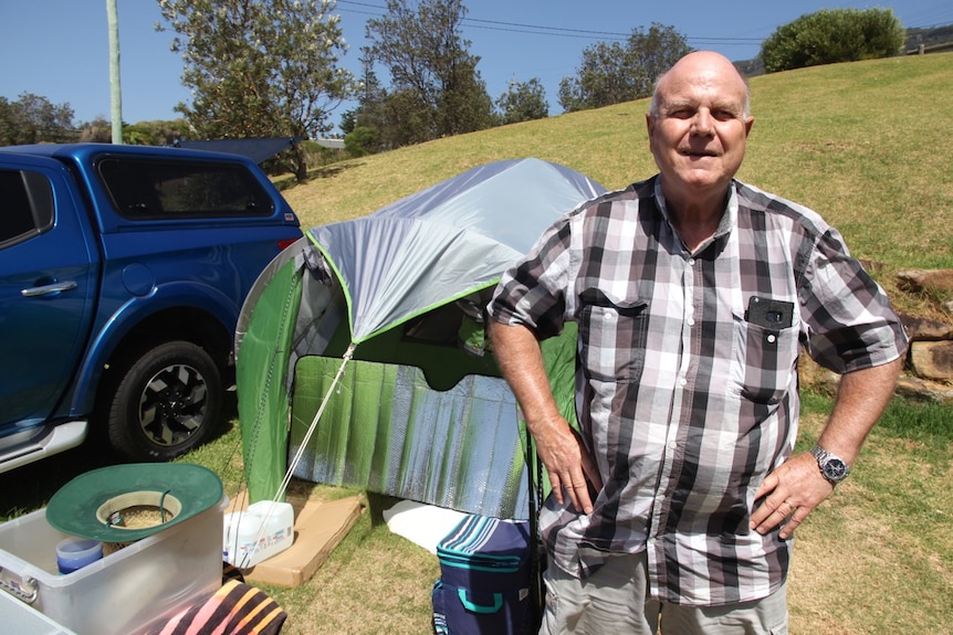 Peter Nicholls stands in front of his tent, at Coledale beach