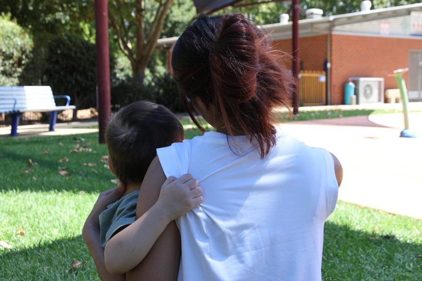 A woman holding a young boy in her arms with their back facing the camera.