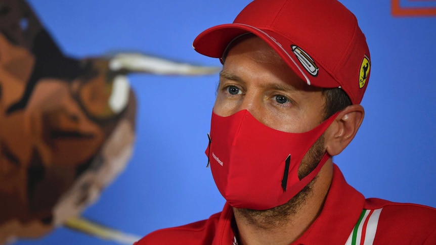 Sebastian Vettel wears a red hat and red facemask in front of a blue background