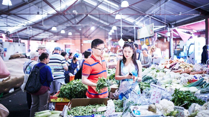 Dua orang sedang membeli sayuran hijau di pasar tradisional