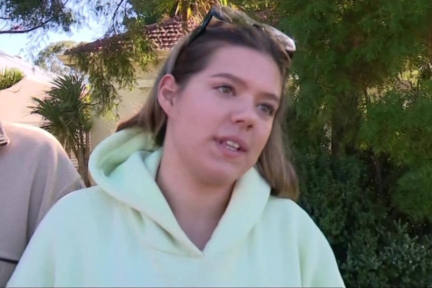 A young woman in a hoodie speaks to reporters.