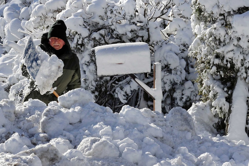A man shovels his driveway which is buried in snow.