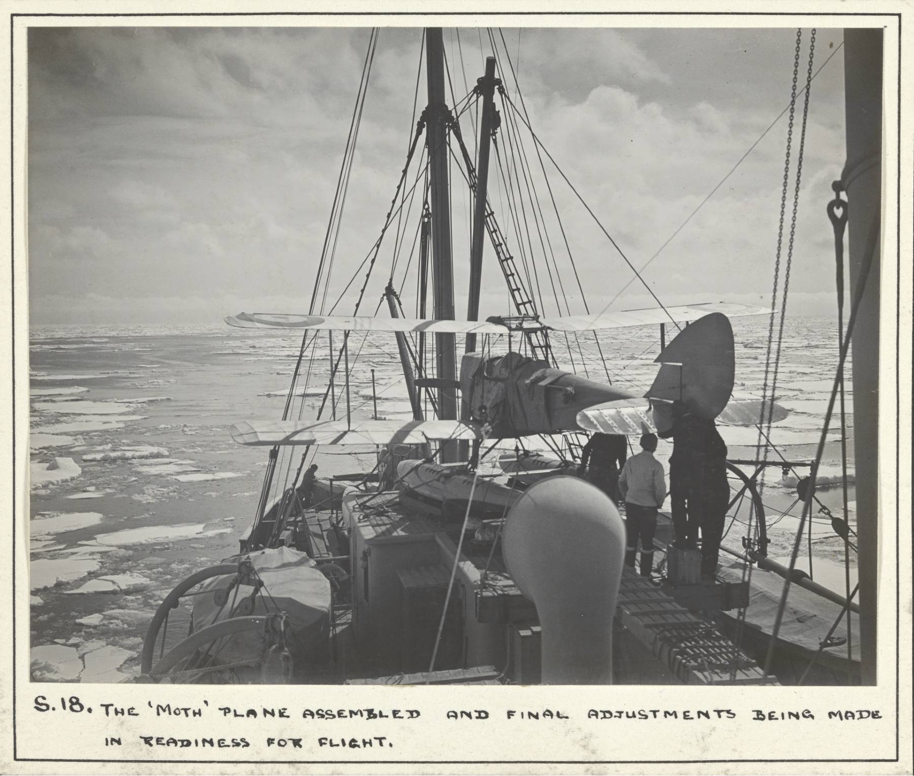 A seaplane sits on the deck of a ship. Icebergs can be seen in the ocean.