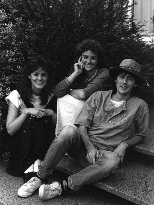 Two young women and a young man sit on a step.