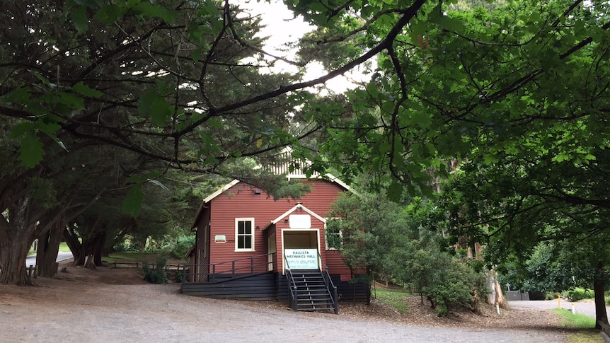 A red weatherboard hall surrounded by trees