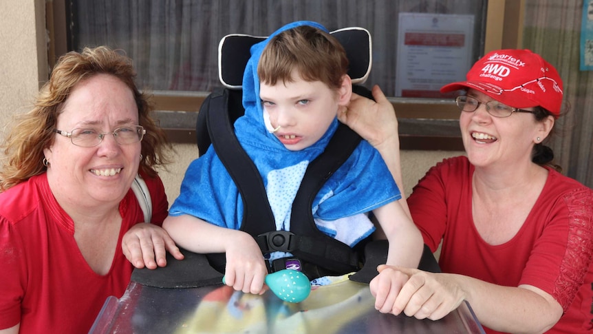 two ladies in red t-shirts crouching next to boy in the middle in a wheelchair