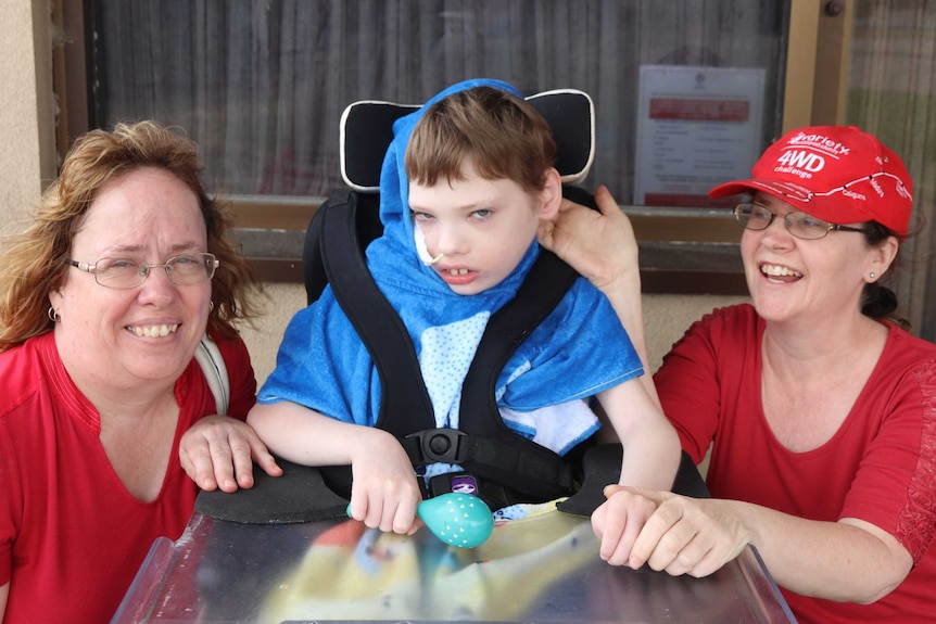 two ladies in red t-shirts crouching next to boy in the middle in a wheelchair