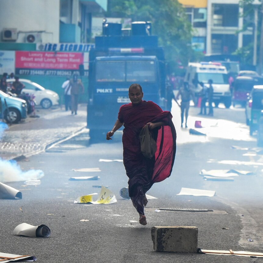 A Buddhist monk runs along a street to escape a cloud of tear gas during a protest