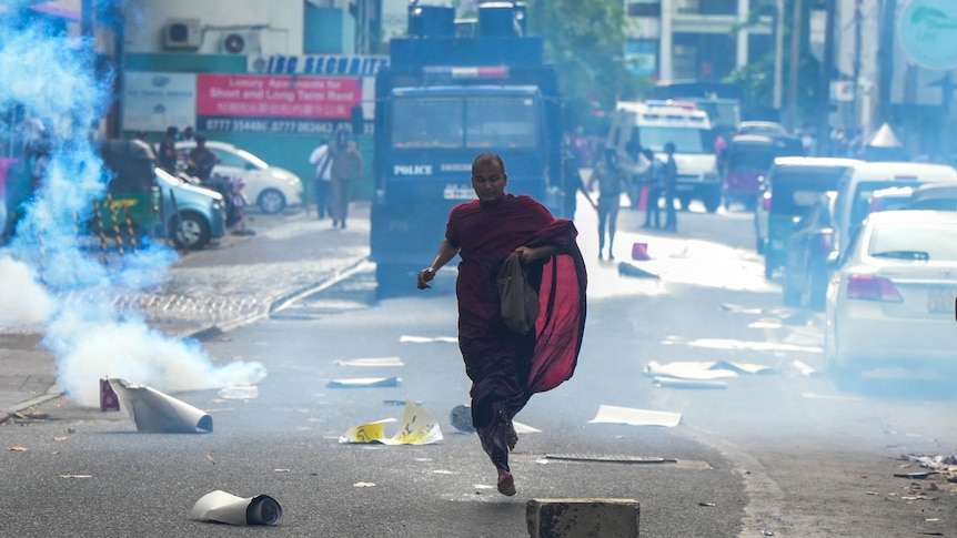 A Buddhist monk runs along a street to escape a cloud of tear gas during a protest