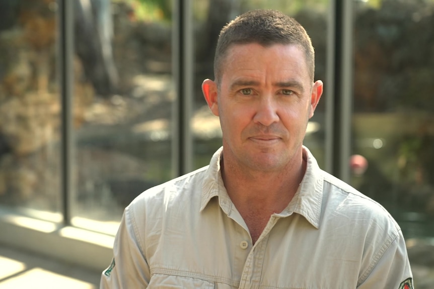 Man in khaki shirt with short hair looks directly at camera.