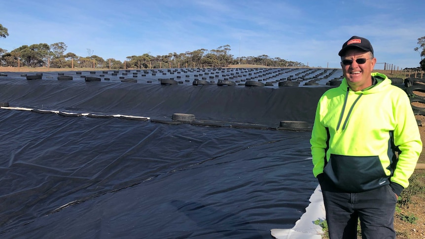 A male farmer Mark Hannemann stands in front of his dam on his property that captures water for his livestock.