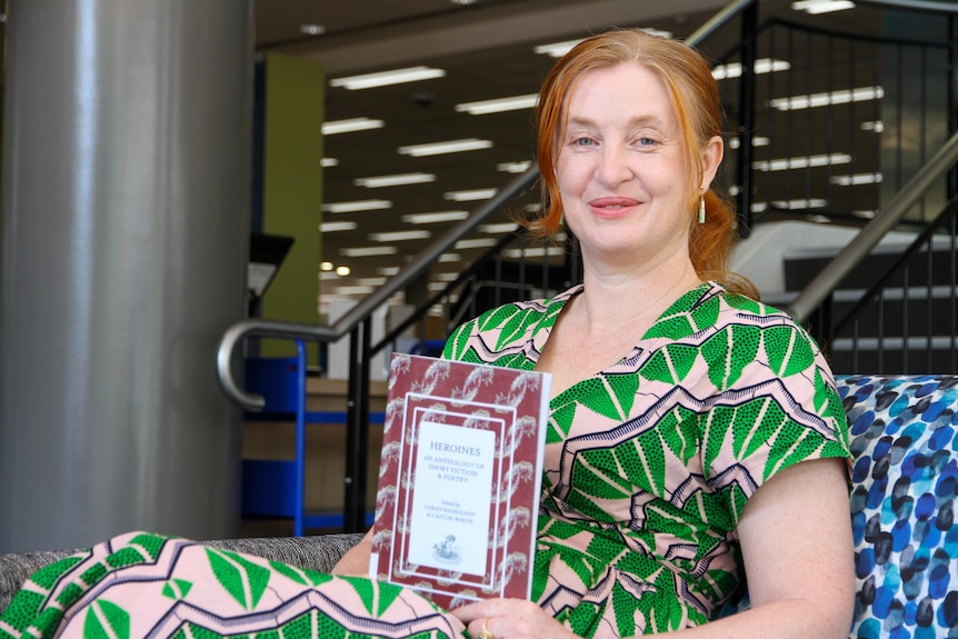 Sarah Nicholson sits holding Volume 4 of Heroines Anthology at Wollongong Library. 