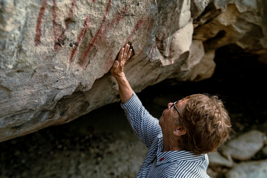 Aboriginal elder Aunty Barbara Simms places her hand in a crevice high up on a cave wall.