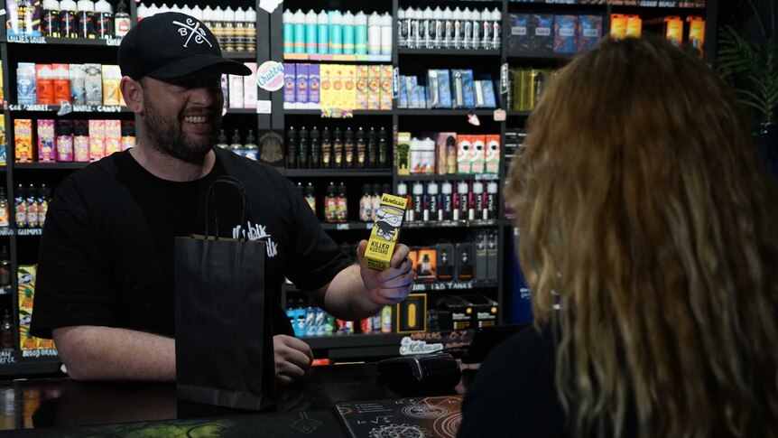 A shopkeeper sells a vaping product to a woman.