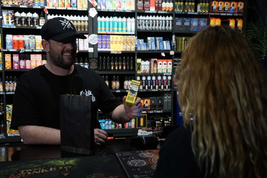 A shopkeeper sells a vaping product to a woman.