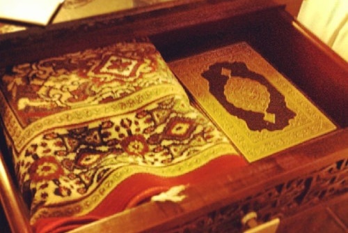A Quran and a prayer rug in a wooden box