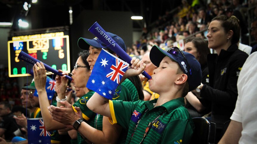 A young boy blows a novelty trumpet with an Australian flag hanging from it.
