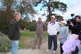 Two Japanese men, and a woman talk with an Australian man in a garden while a tv cameraman is filming