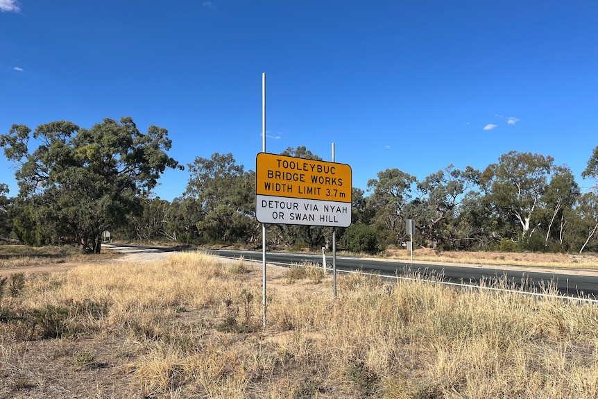 A yellow road sign next to a road.