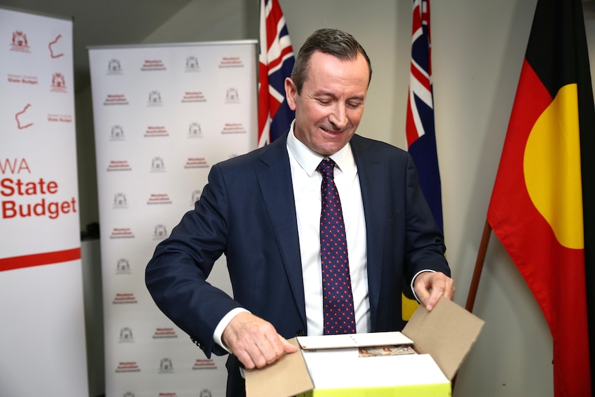 Mark McGowan looking down at a box of budget papers as he opens it up.