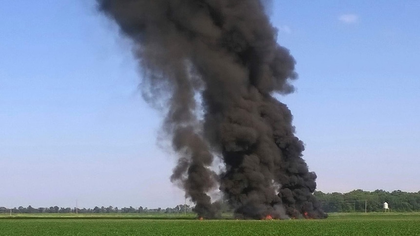 Thick black smoke rises from flames on a field.