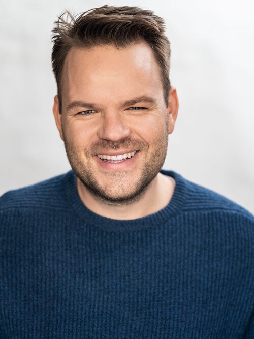 Portrait of a man in a navy jumper smiling.